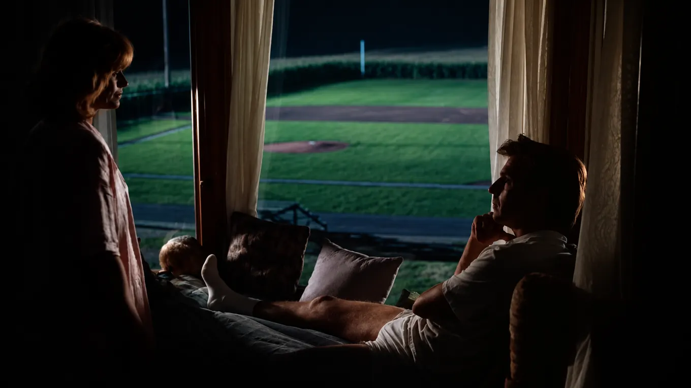 A couple sharing a quiet moment beside a baseball field at night.